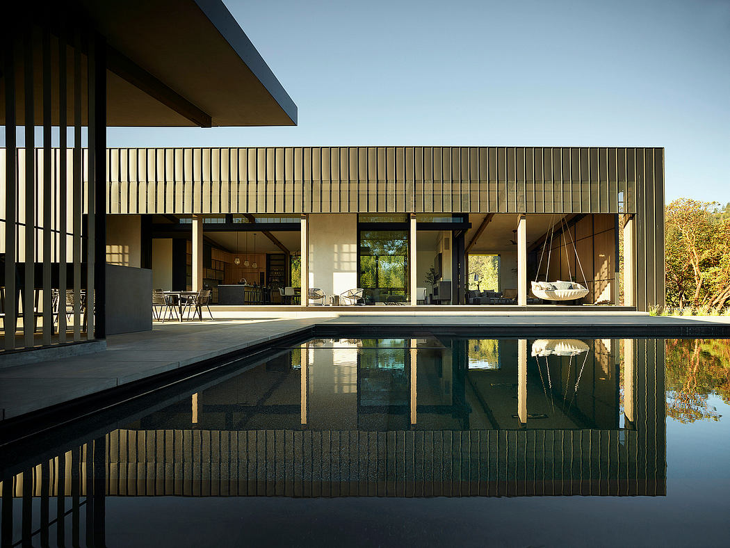 A modern, minimalist house with a pool reflecting the wooden slatted facade and natural surroundings.