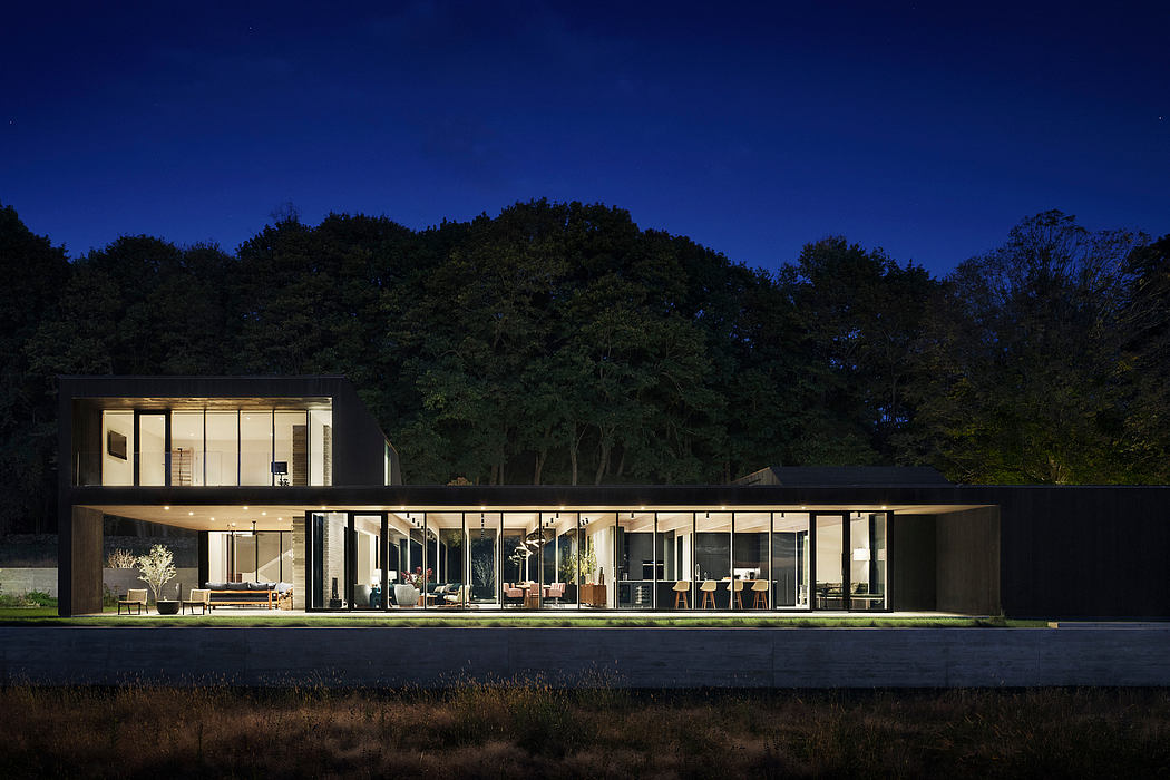 Expansive modern glass-walled home nestled in a wooded landscape at night.