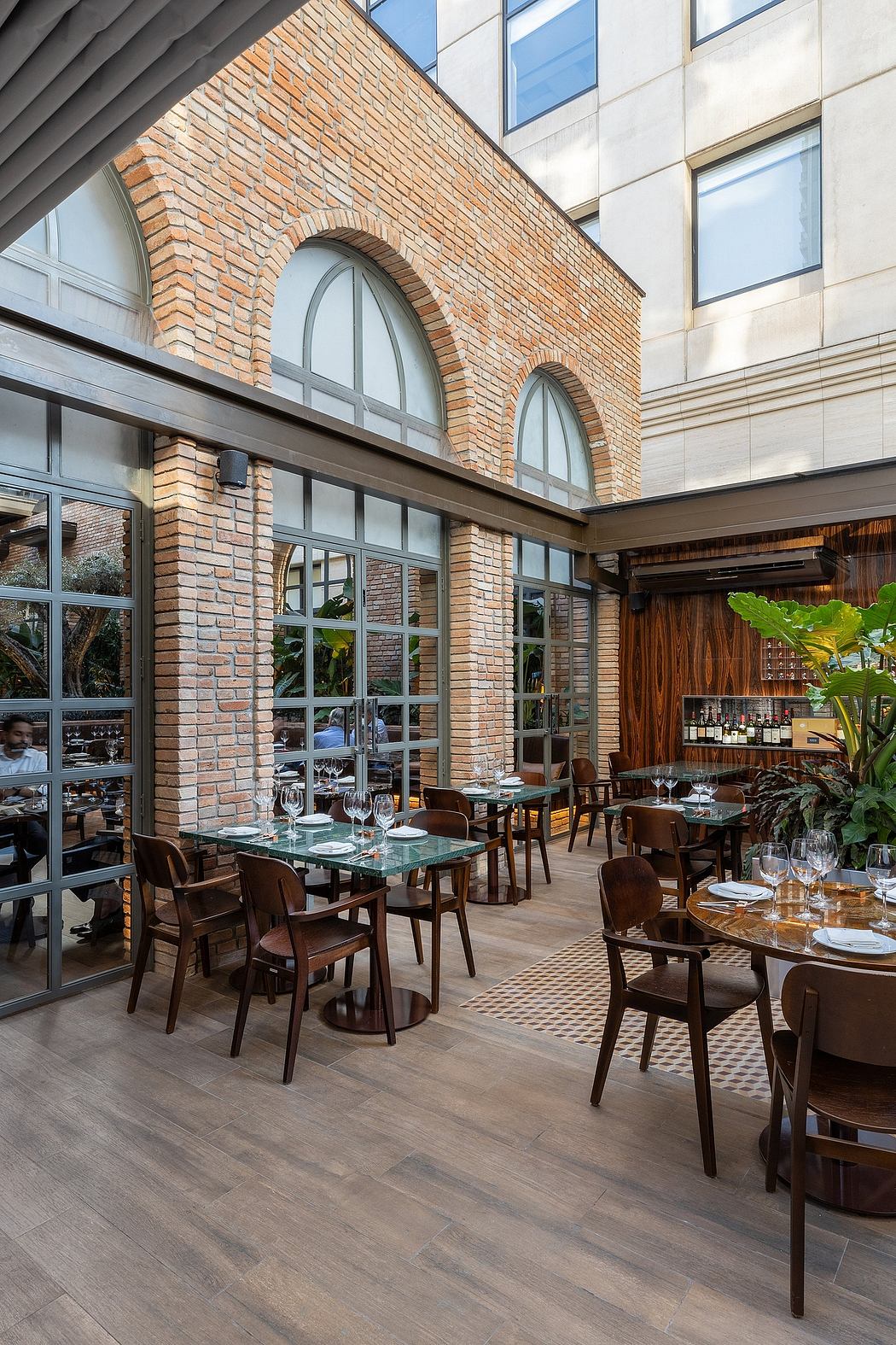 Modern restaurant interior with arched brick walls, large windows, and wooden furniture.