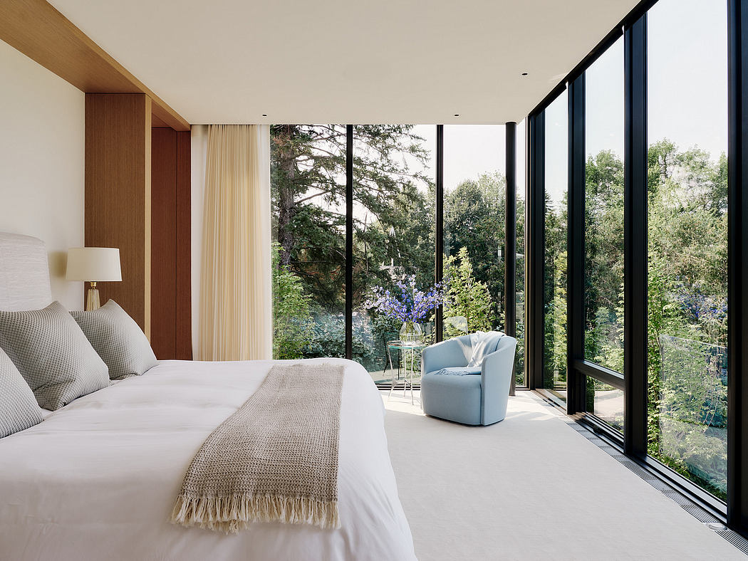 Modern bedroom with expansive windows overlooking a lush, natural landscape.