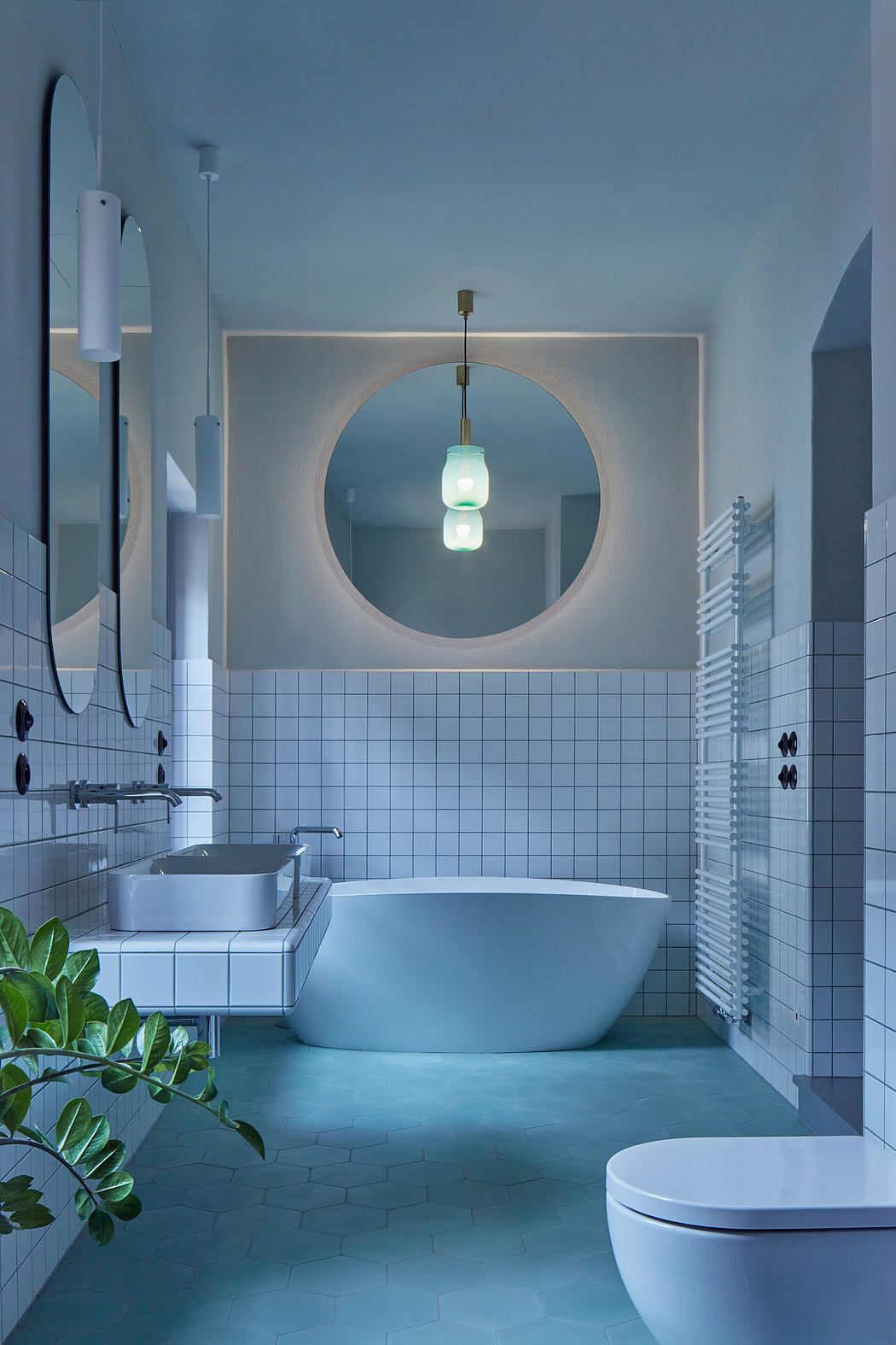 A modern bathroom with a circular mirror, pendant lighting, and a freestanding tub.
