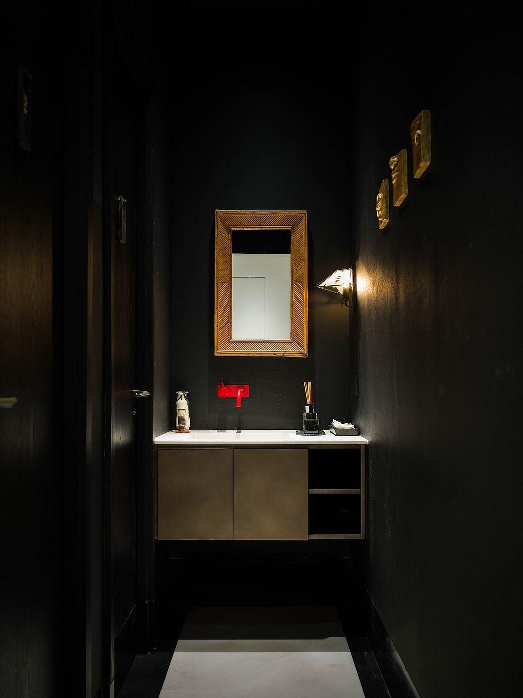 Minimalist bathroom vanity with gilded mirror frame and subtle lighting against dark walls.