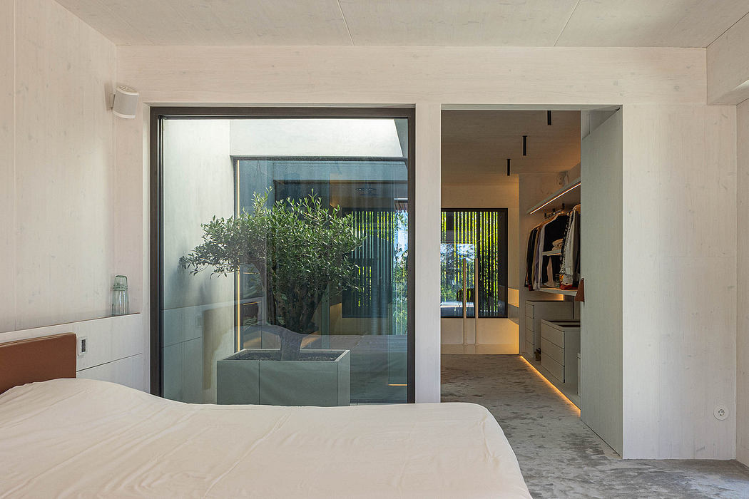 Modern bedroom with sliding glass doors framing a potted plant and leading to an open interior space.