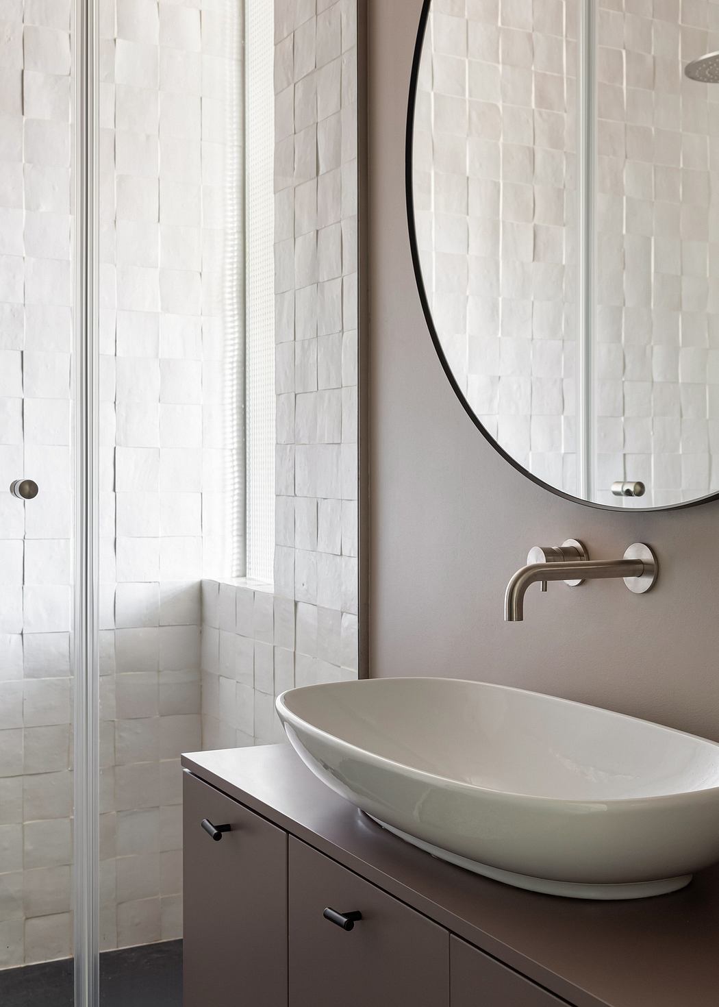 A contemporary bathroom with a sleek oval sink, black framed mirror, and textured tile walls.
