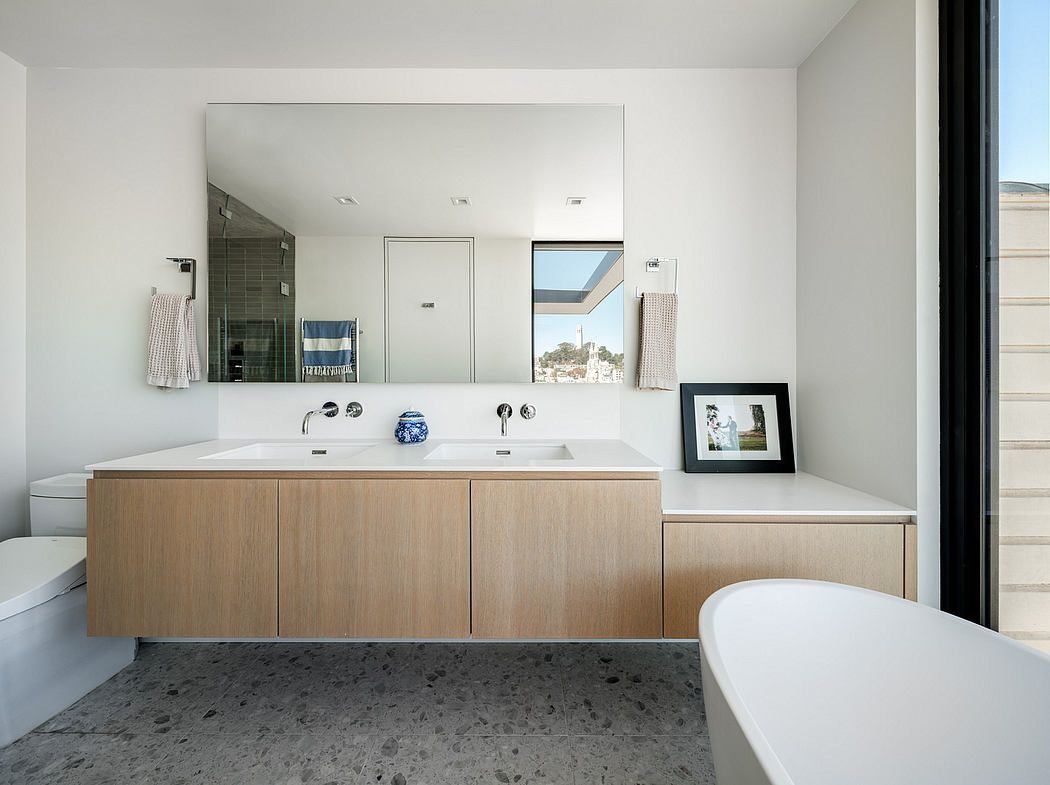 Modern bathroom with sleek white walls, double sinks, and wood vanity, accented by black-and-white framed artwork.