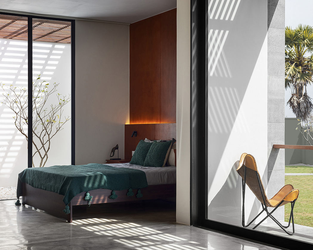 Minimalist bedroom with warm lighting, textured walls, and sleek furnishings overlooking lush greenery.