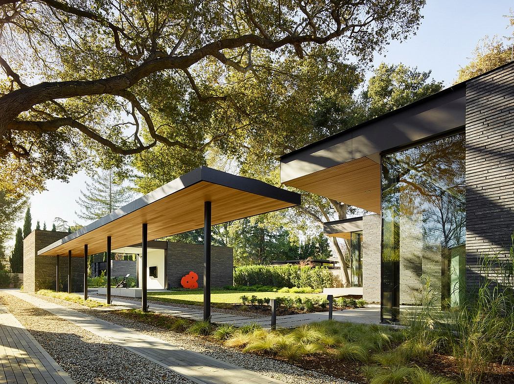 A modern, glass-walled building with a low-pitched roof nestled among lush, mature trees.