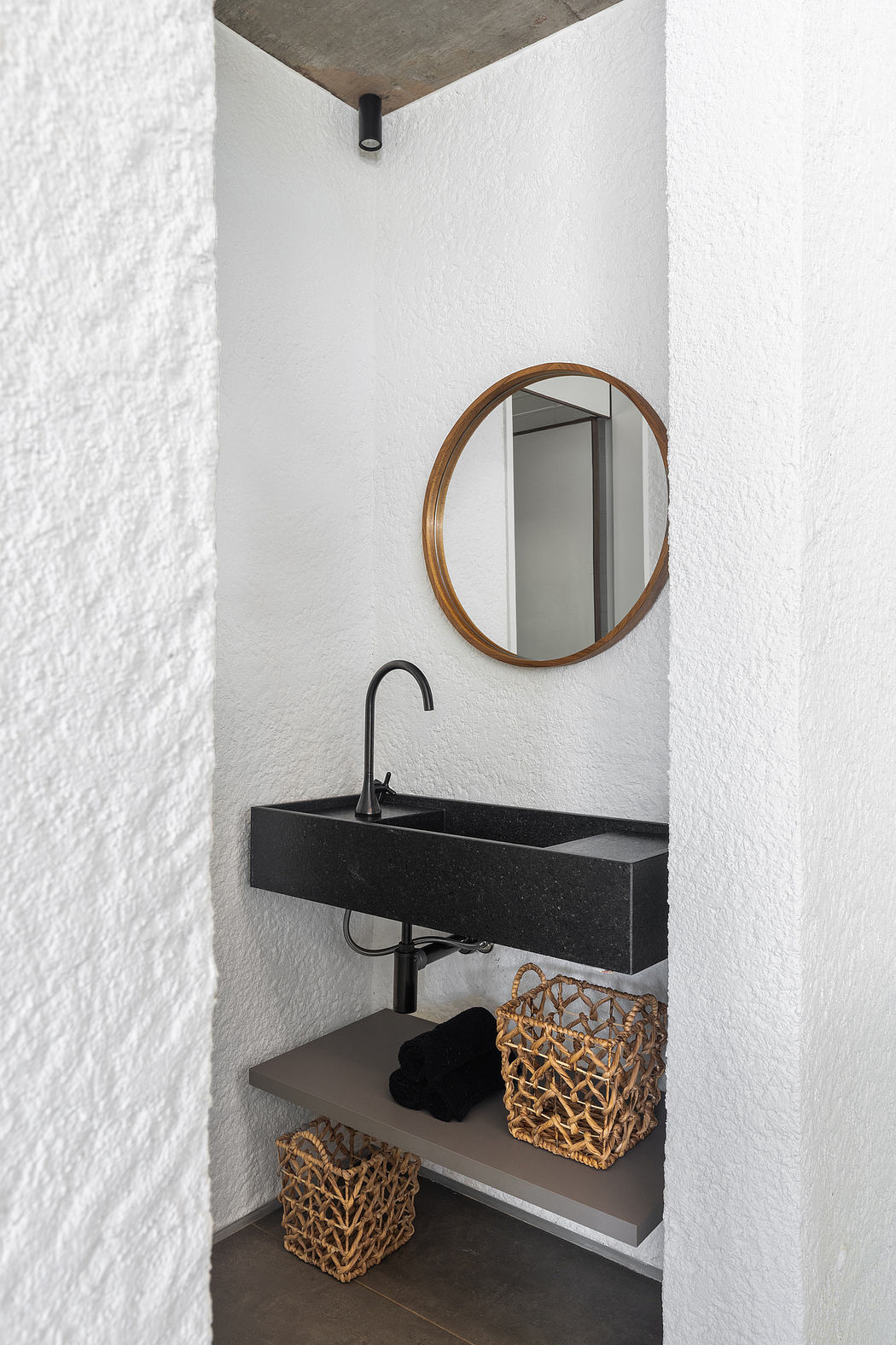 A minimalist bathroom with a round mirror, black sink, and woven baskets for storage.