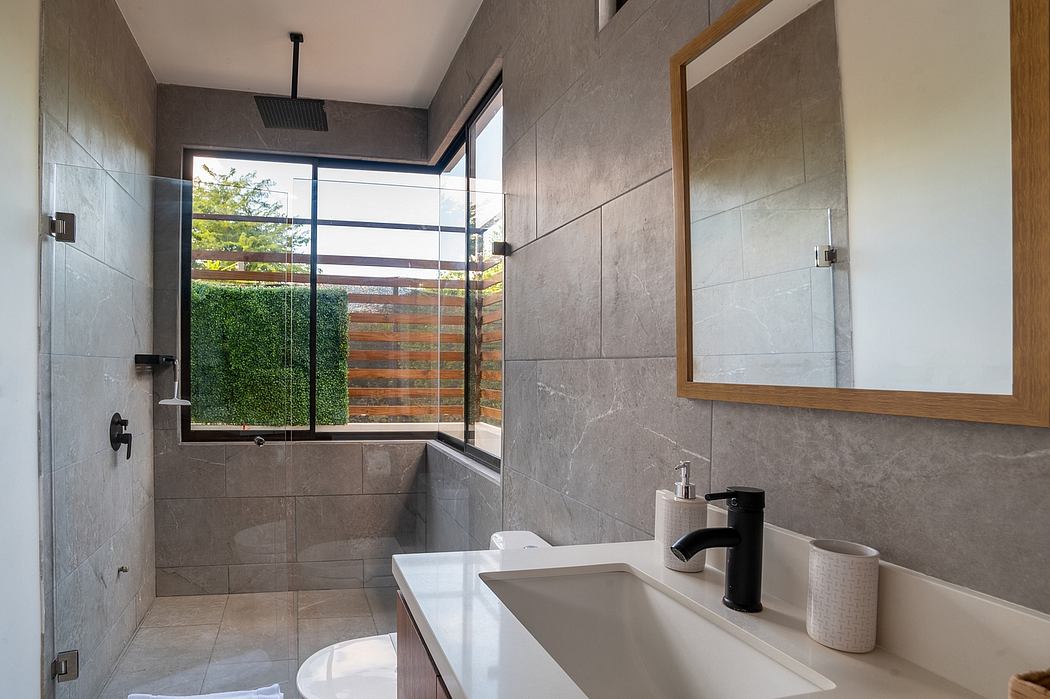 A modern, minimalist bathroom with gray tiles, a vanity, and a large window overlooking greenery.