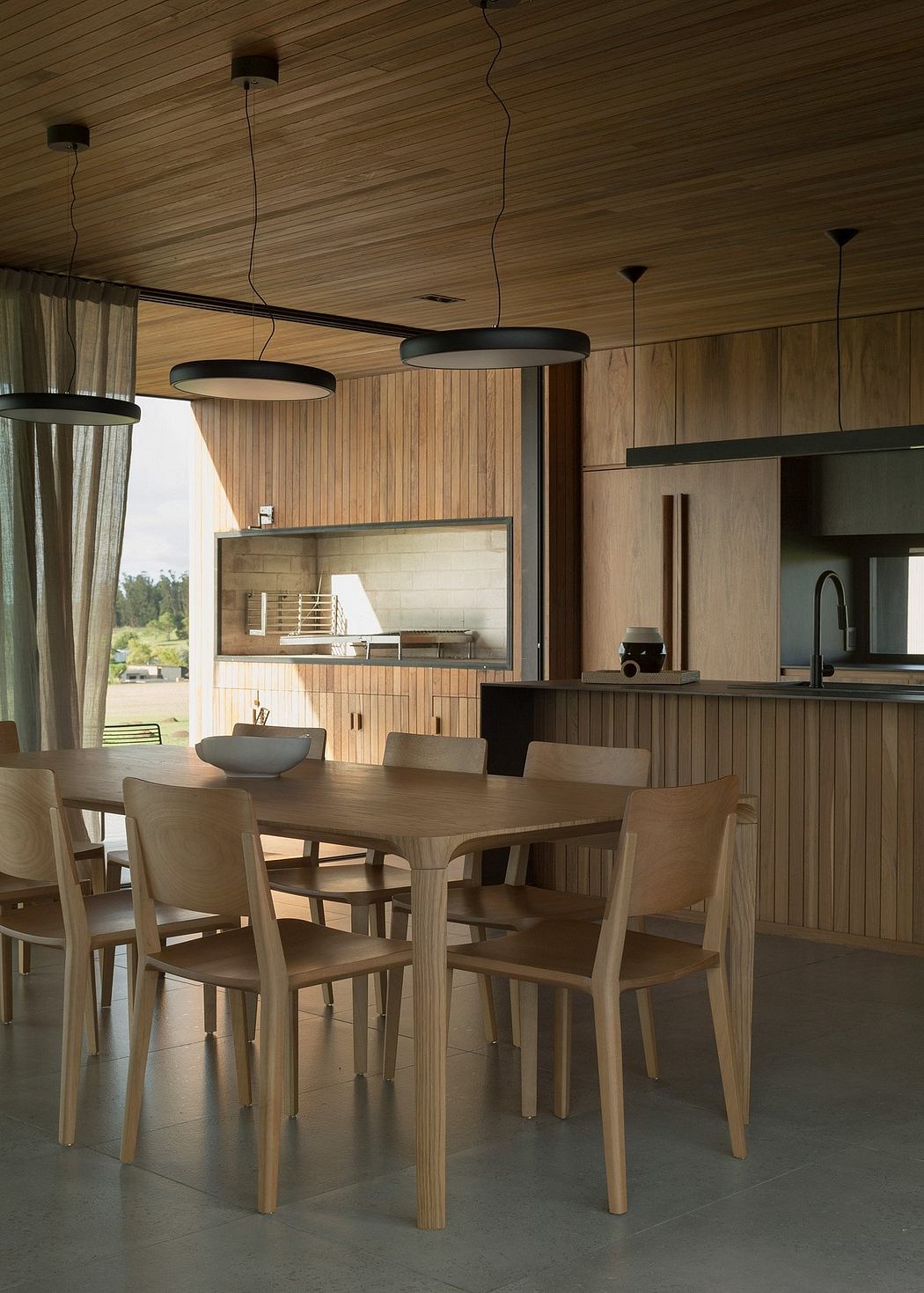 Minimalist wooden dining room with sleek light fixtures and open kitchen design.