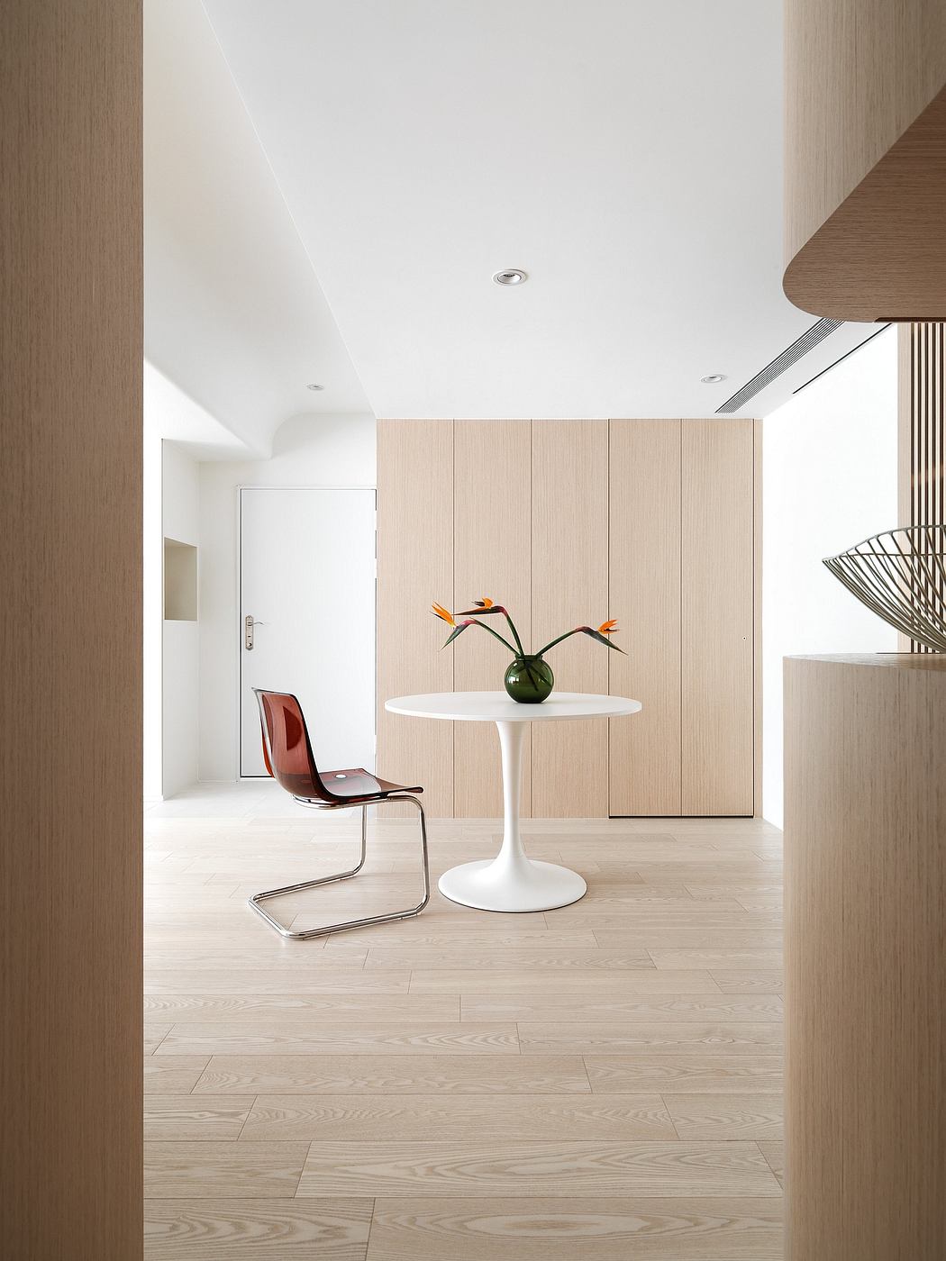 Minimalist interior with white table, red chair, and built-in wooden cabinetry.