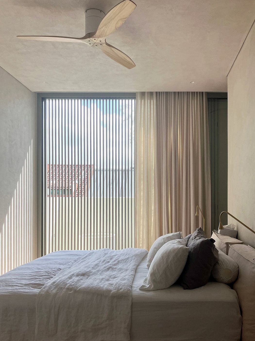Large window with vertical blinds, soft lighting, and a modern ceiling fan in a minimalist bedroom.