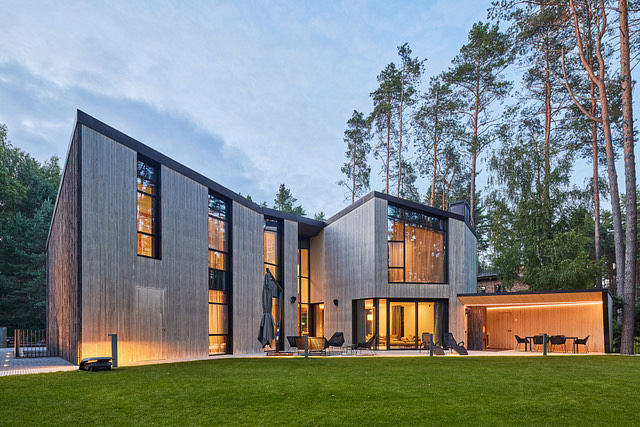 Modern, sleek wooden structure with large windows illuminating the interior and surrounded by a lush green lawn.