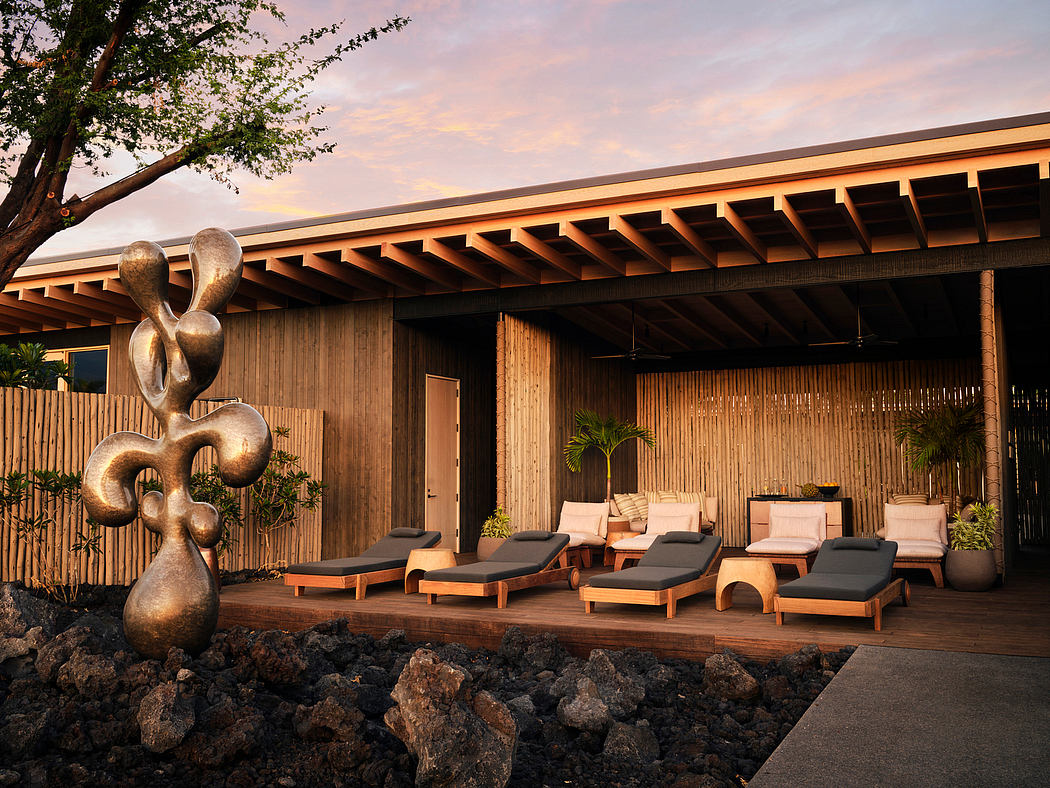 Rustic wooden structure with lounge chairs and an abstract metal sculpture at sunset.