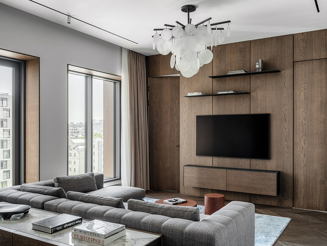 Expansive modern living room with wood-paneled walls, plush grey sofa, and elegant chandelier.