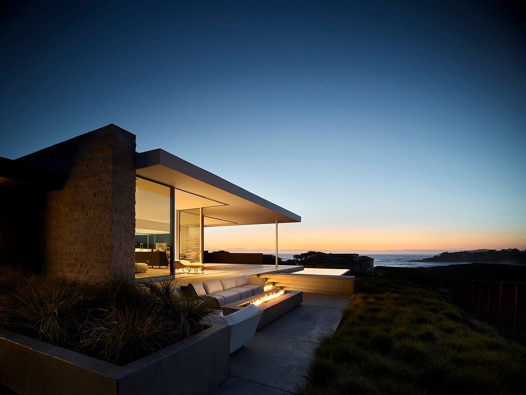Sleek, modern home with open-air patio, stone walls, and panoramic ocean views at sunset.