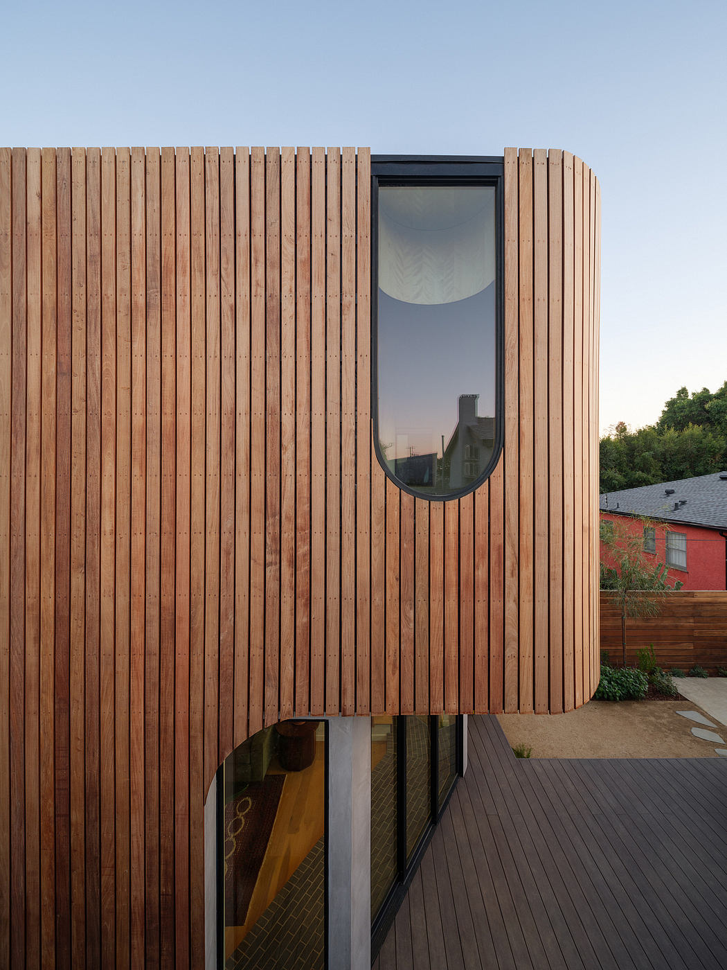 Wooden slat facade with oval window, elevated deck, and surrounding landscape.