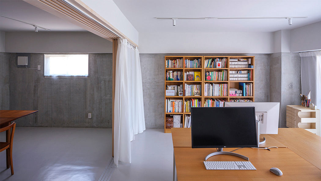 Large bookshelf with diverse collection, modern desk setup, and white curtains in room.