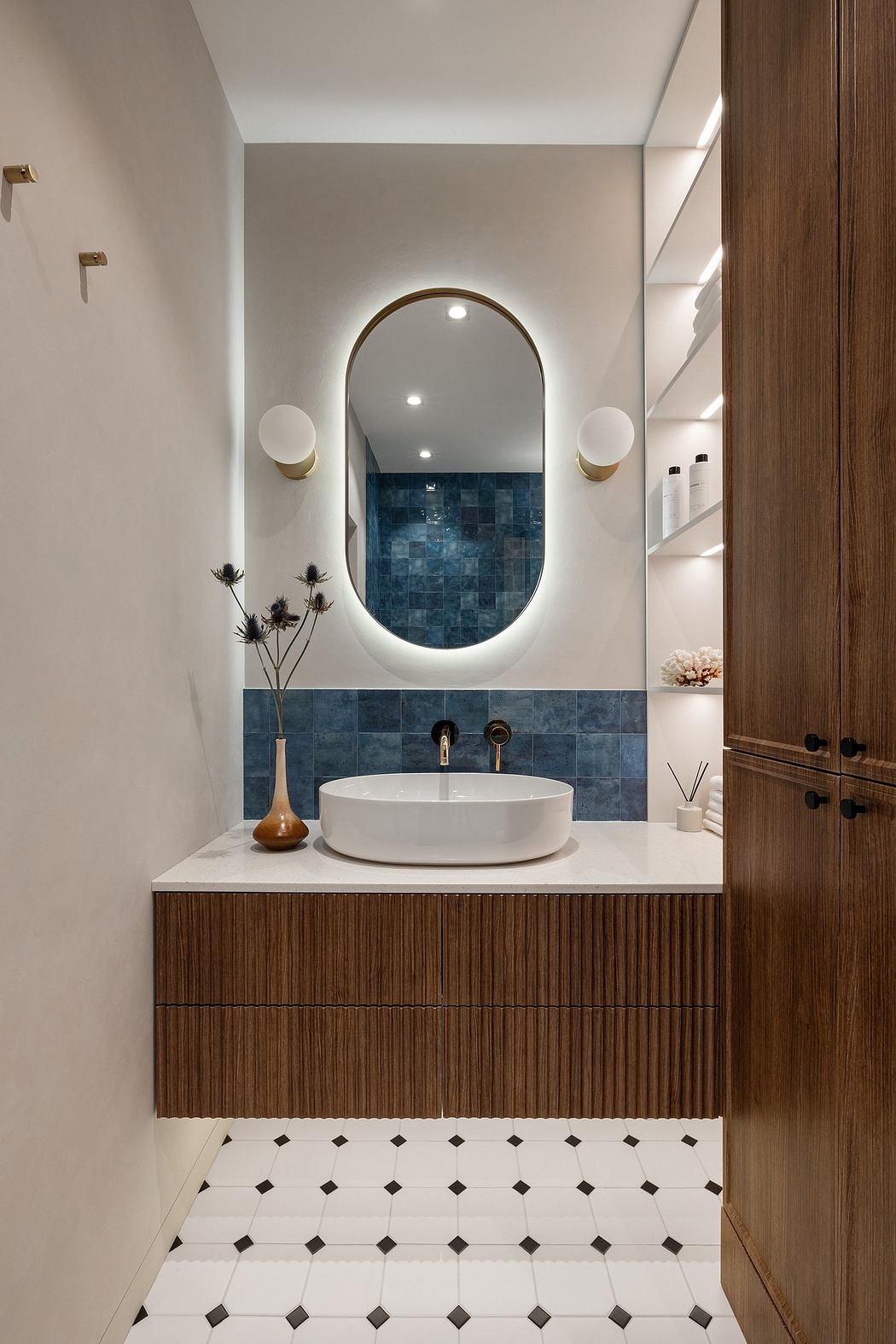 A modern bathroom with a white sink, oval mirror, and blue tile backsplash. Wooden vanity drawers.