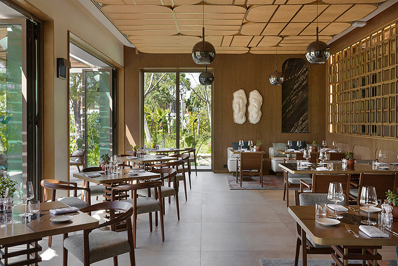 Warm-toned interior with wooden furniture, patterned ceiling, and floor-to-ceiling windows.