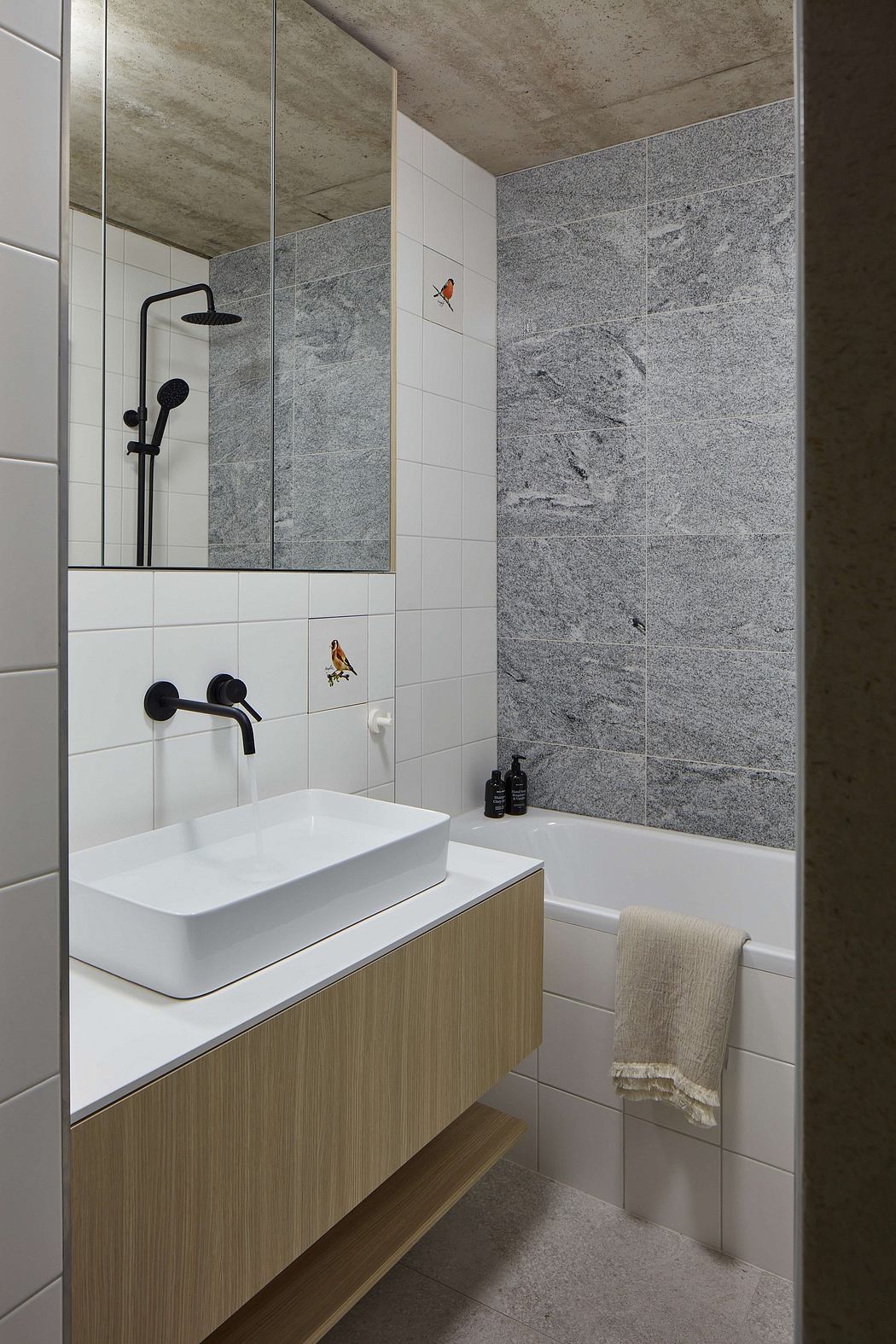 A modern bathroom with a white sink, wooden vanity, and gray tiled walls and floor.