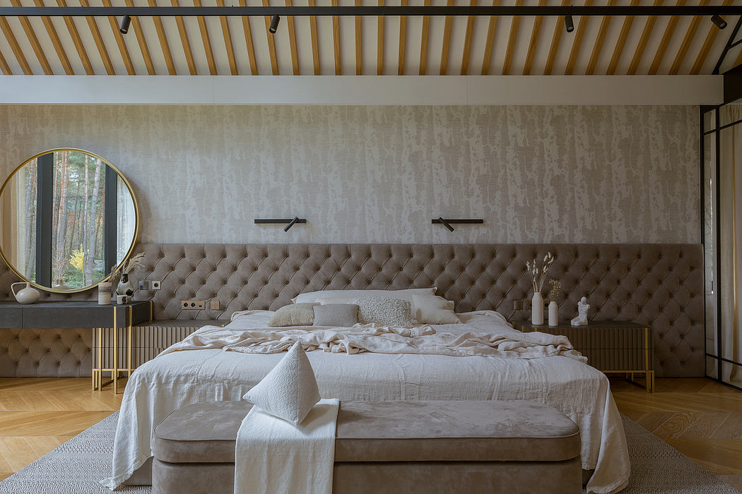 Cozy, modern bedroom with tufted headboard, round mirror, and exposed timber ceiling.