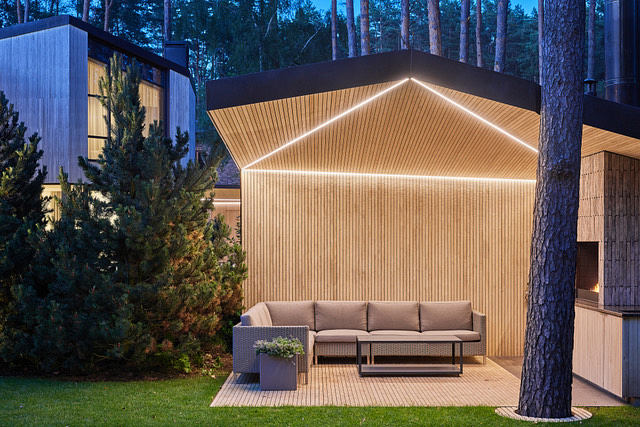 Modern outdoor living space with illuminated geometric wooden structure and comfortable lounge furniture.