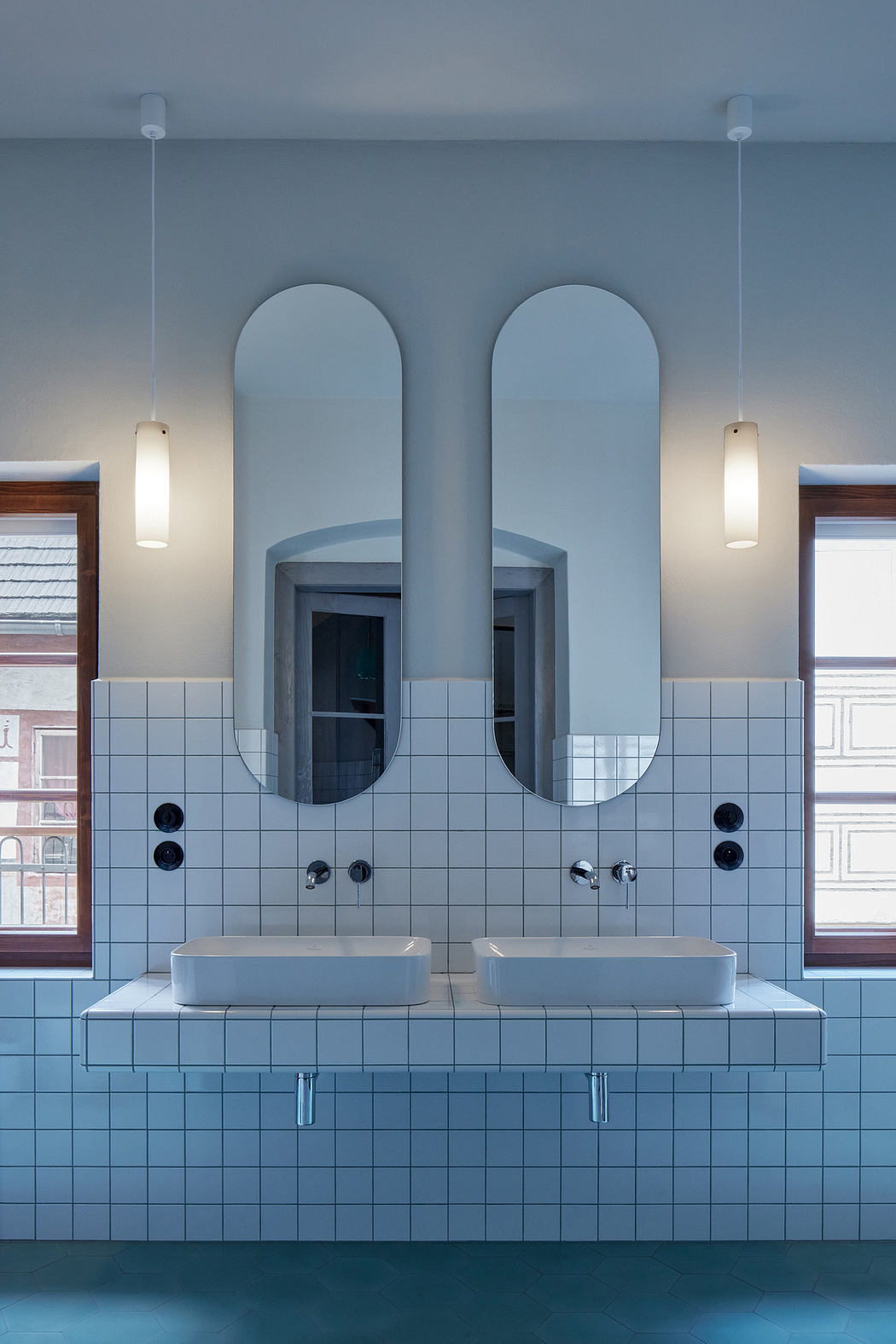Modern bathroom with arched mirrors, tiled walls, and floating vanity sinks.