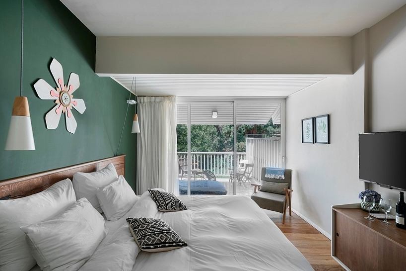 Cozy bedroom with wooden floors, large window, and green accent wall with decorative flower.