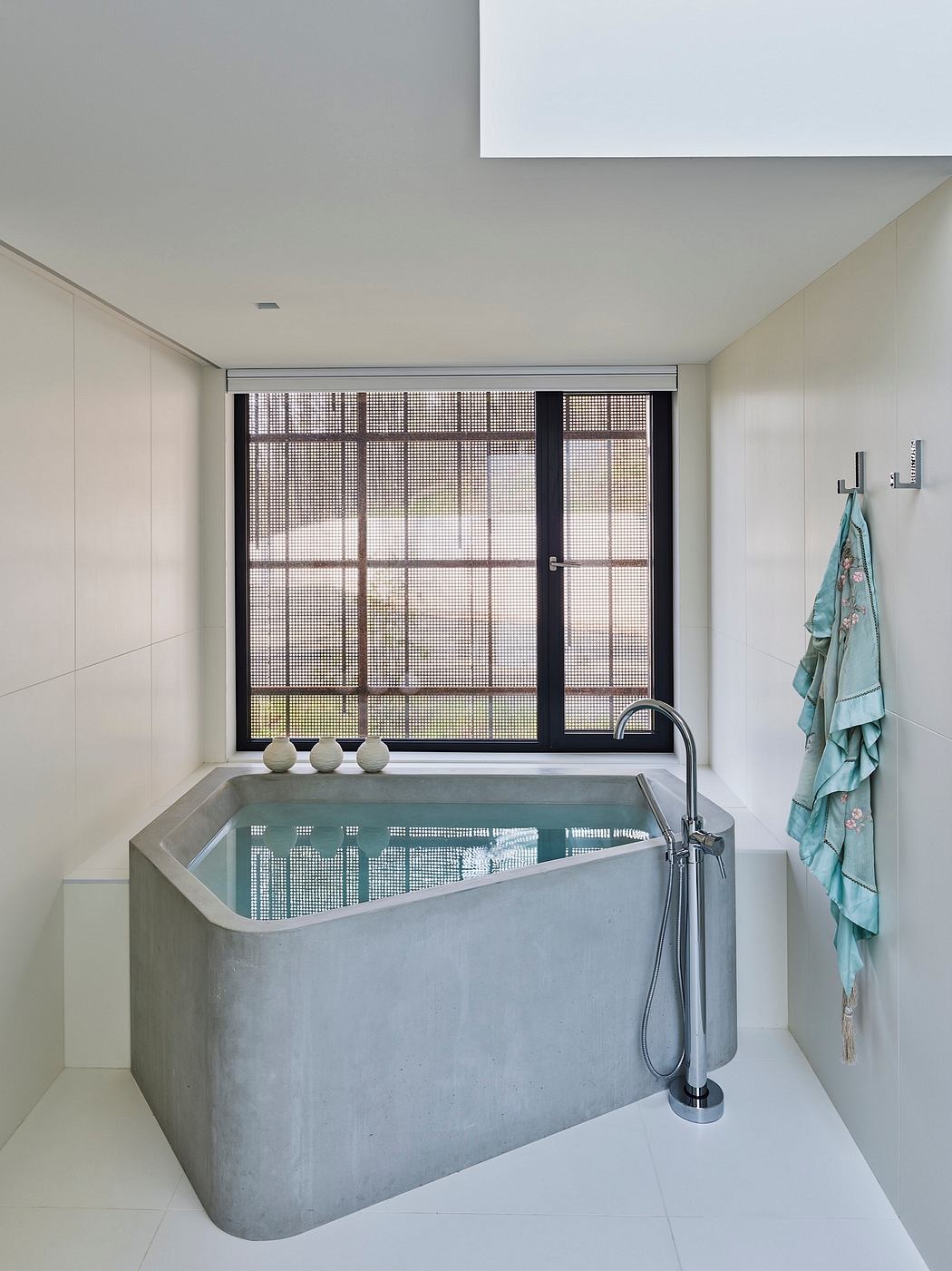 Sleek modern bathroom with minimalist concrete tub, latticed window, and teal towel.