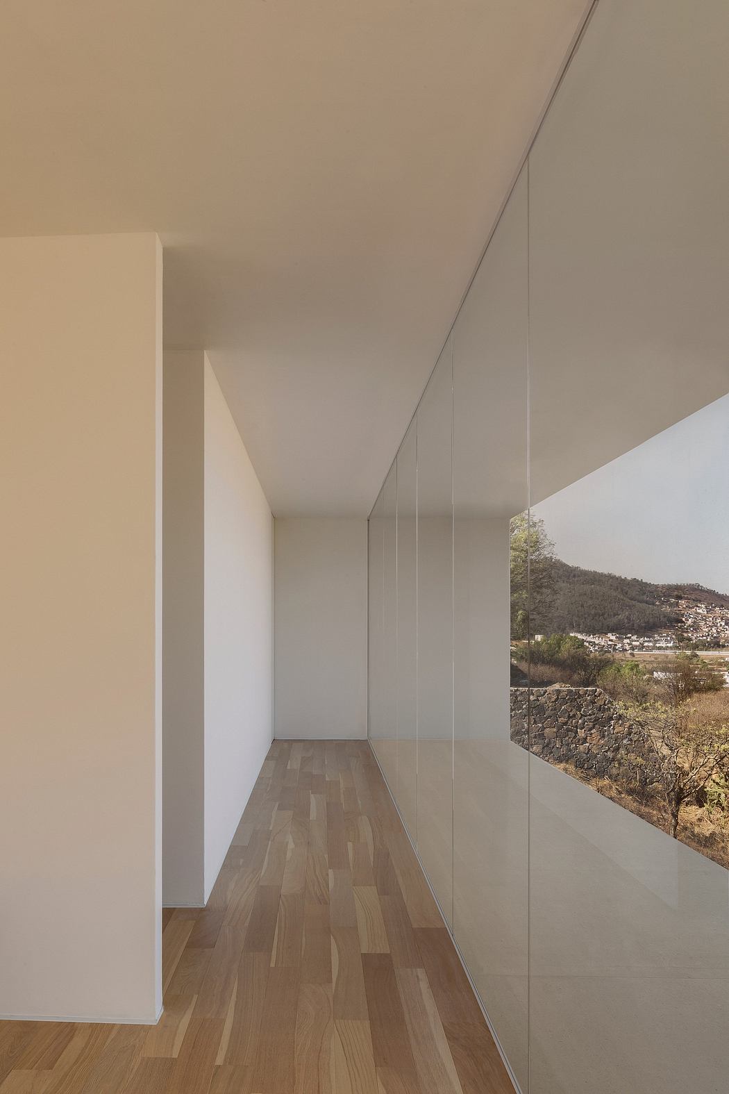 Minimalist interior with clean lines, wood floors, and expansive window overlooking a scenic view.