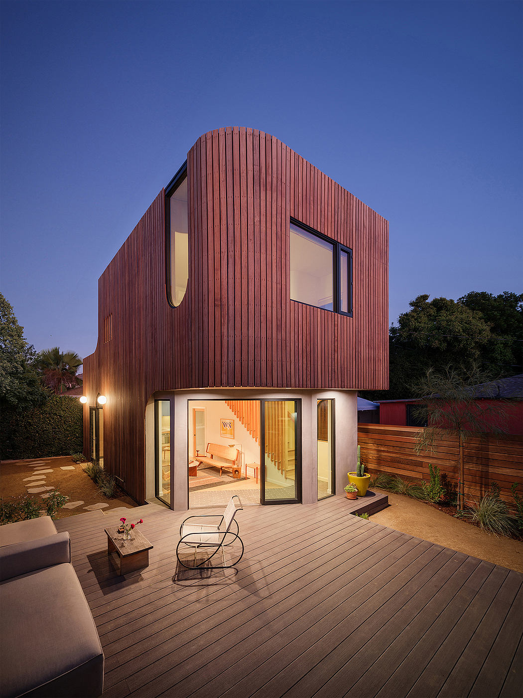 A modern, wooden-clad home with a curved roof, large windows, and a spacious deck.