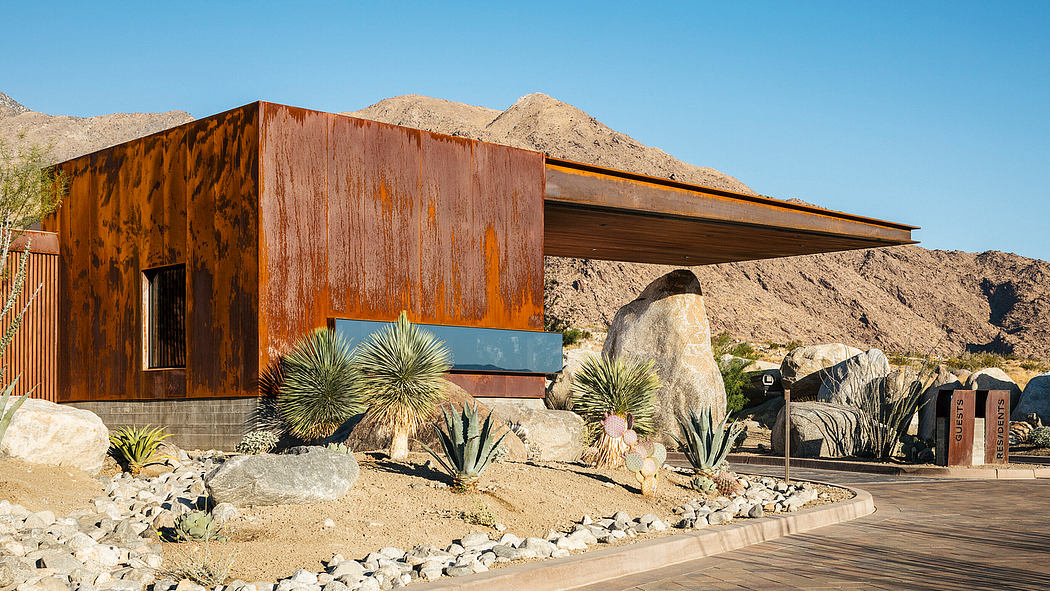 A modern, rustic-style building with a sloped roof, surrounded by desert landscaping and boulders.
