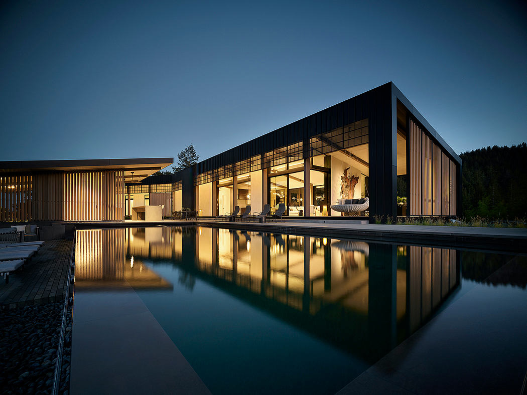 A modern, minimalist building with a large reflective pool and warm interior lighting.
