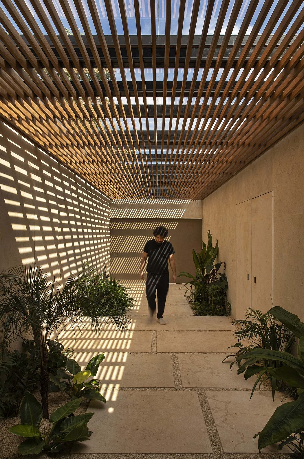 Striking architectural structure with intricate wooden slat ceiling, lush plants, and paved walkway.