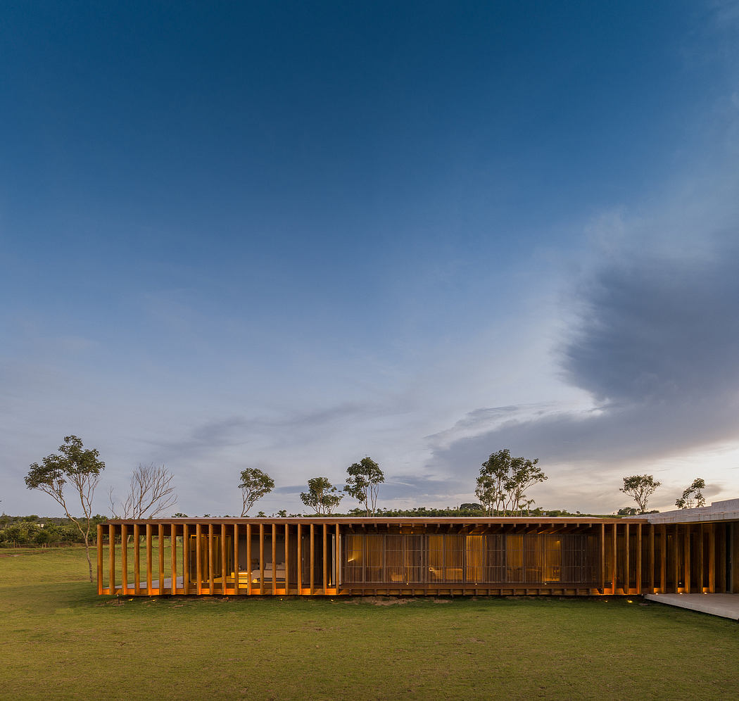 A modern, wooden pavilion with a raised platform overlooking a grassy field and trees.