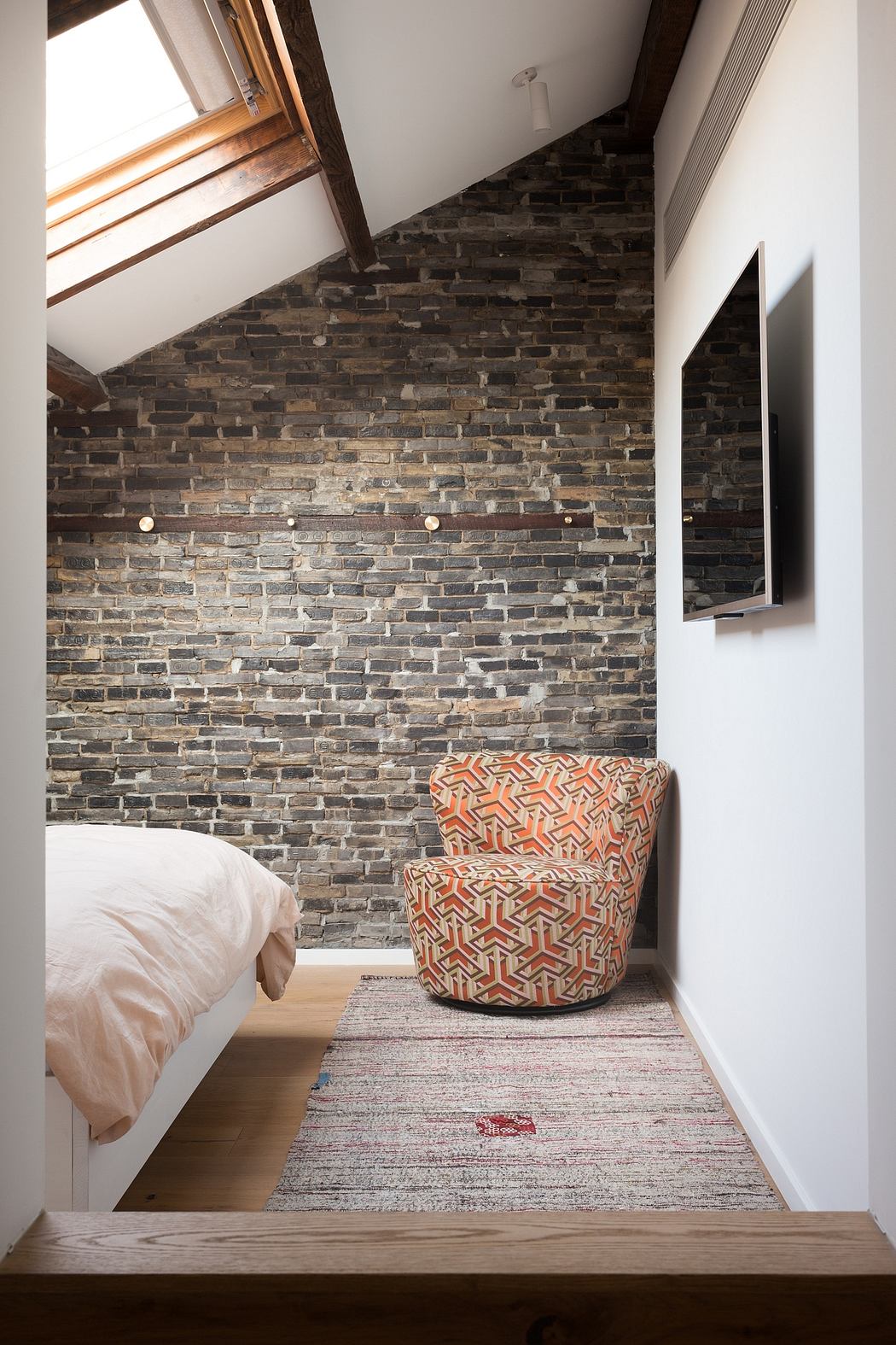 Cozy bedroom with rustic brick wall, patterned armchair, and textured area rug.