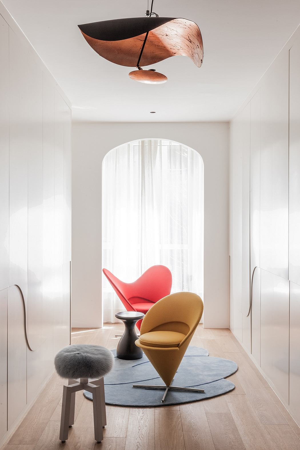 A modern, minimalist living space featuring unique lighting fixture, colorful chairs, and a plush rug.