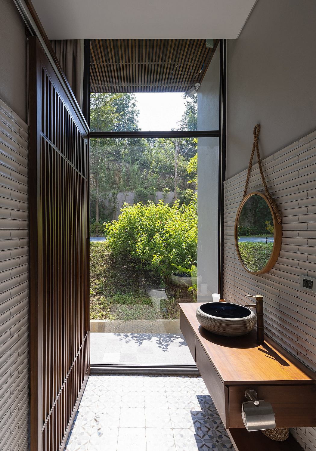 Spacious bathroom with large window overlooking lush greenery, wooden vanity, and round mirror.