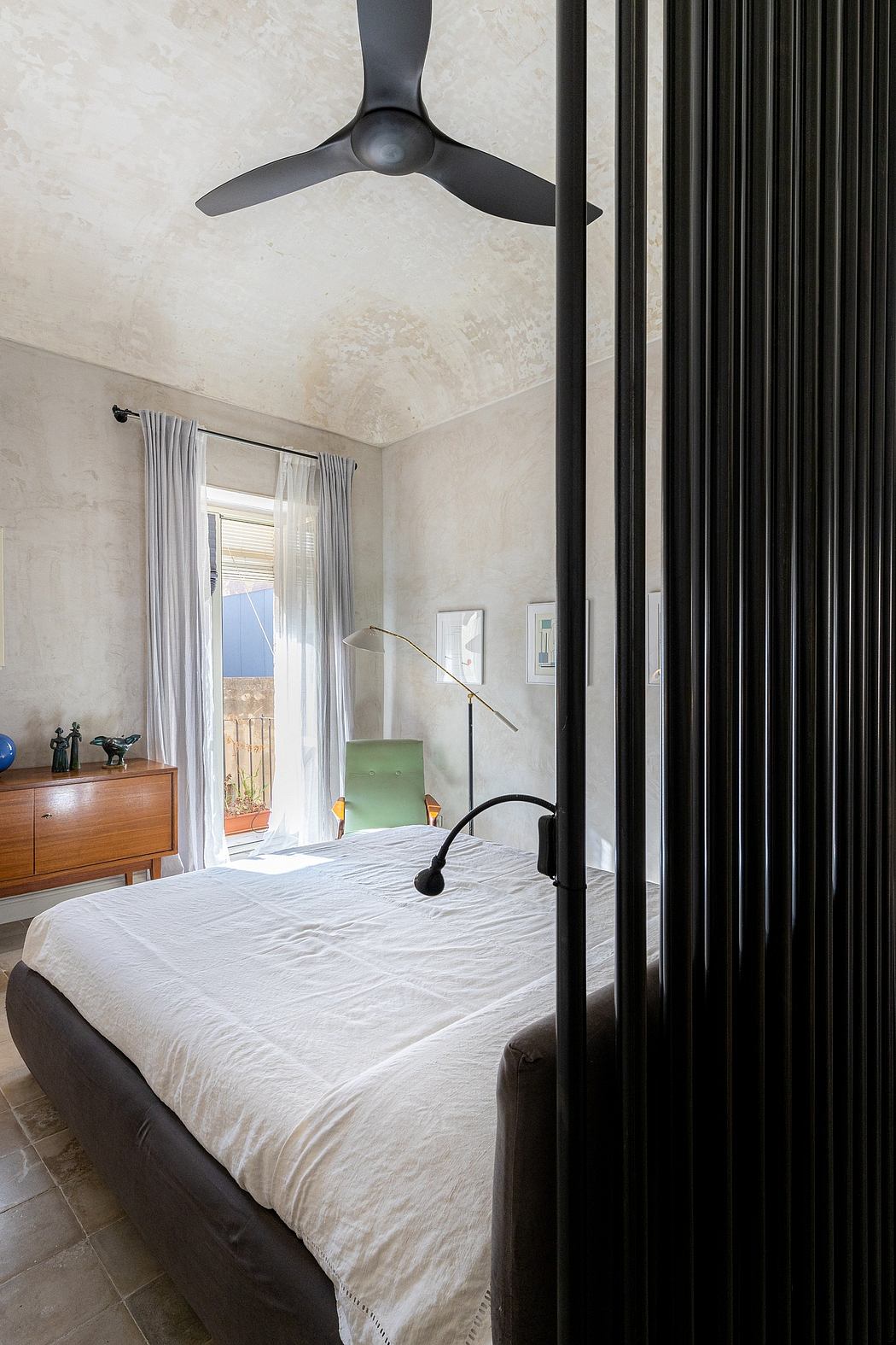 A cozy bedroom with a modern ceiling fan, sleek black curtain rods, and a midcentury dresser.