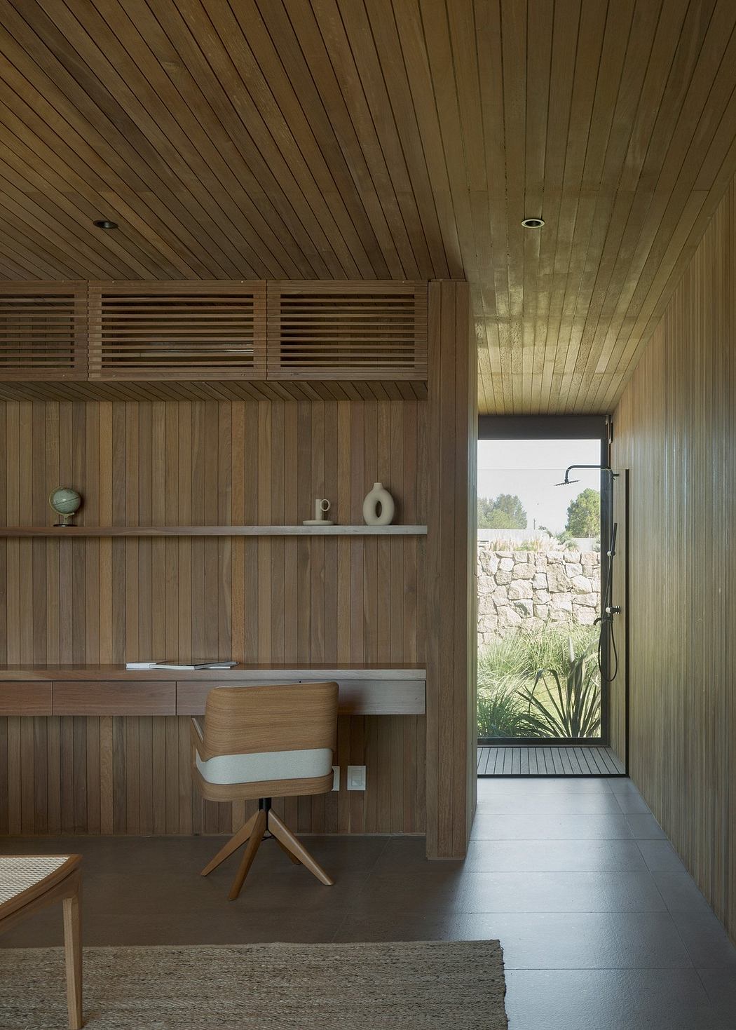 A modern, minimalist interior with wooden walls, shelves, and a swivel chair overlooking a stone exterior.