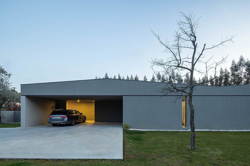 A modern, minimalist garage building with a dark exterior and sleek design. The car inside is visible through the open garage door.