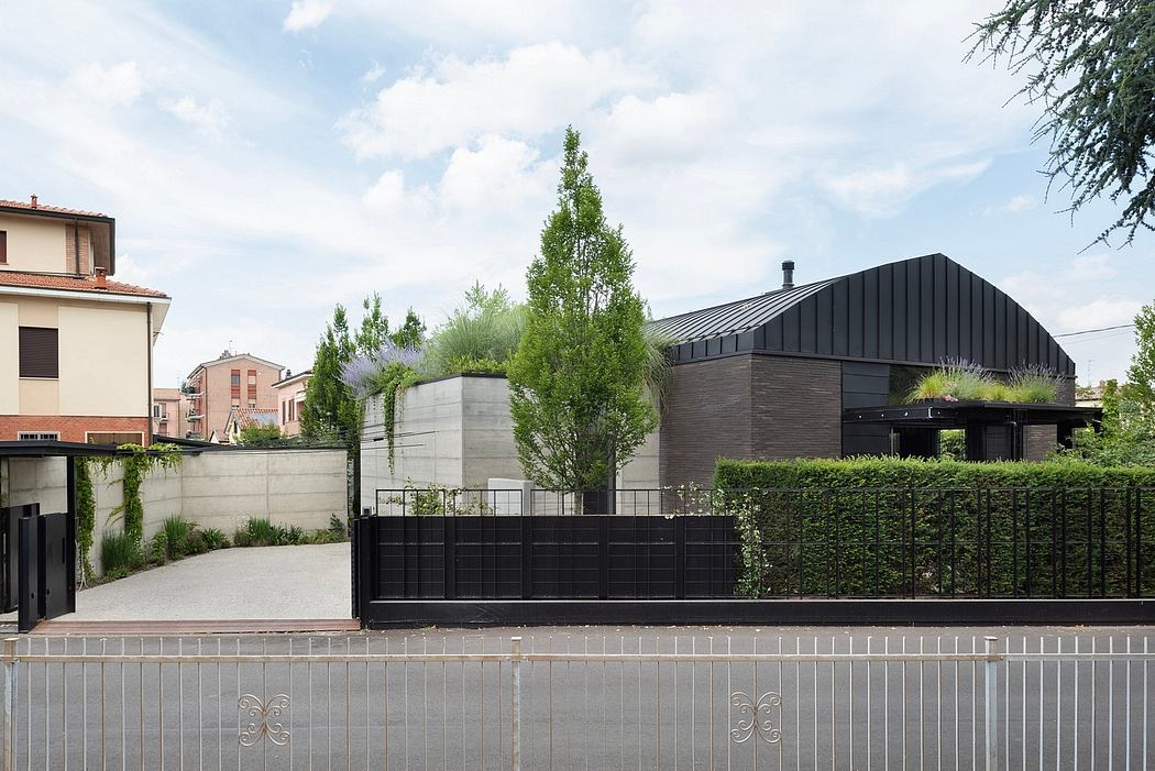 Modern architectural design featuring a black metal building with a gabled roof, surrounded by lush greenery and a decorative metal fence.