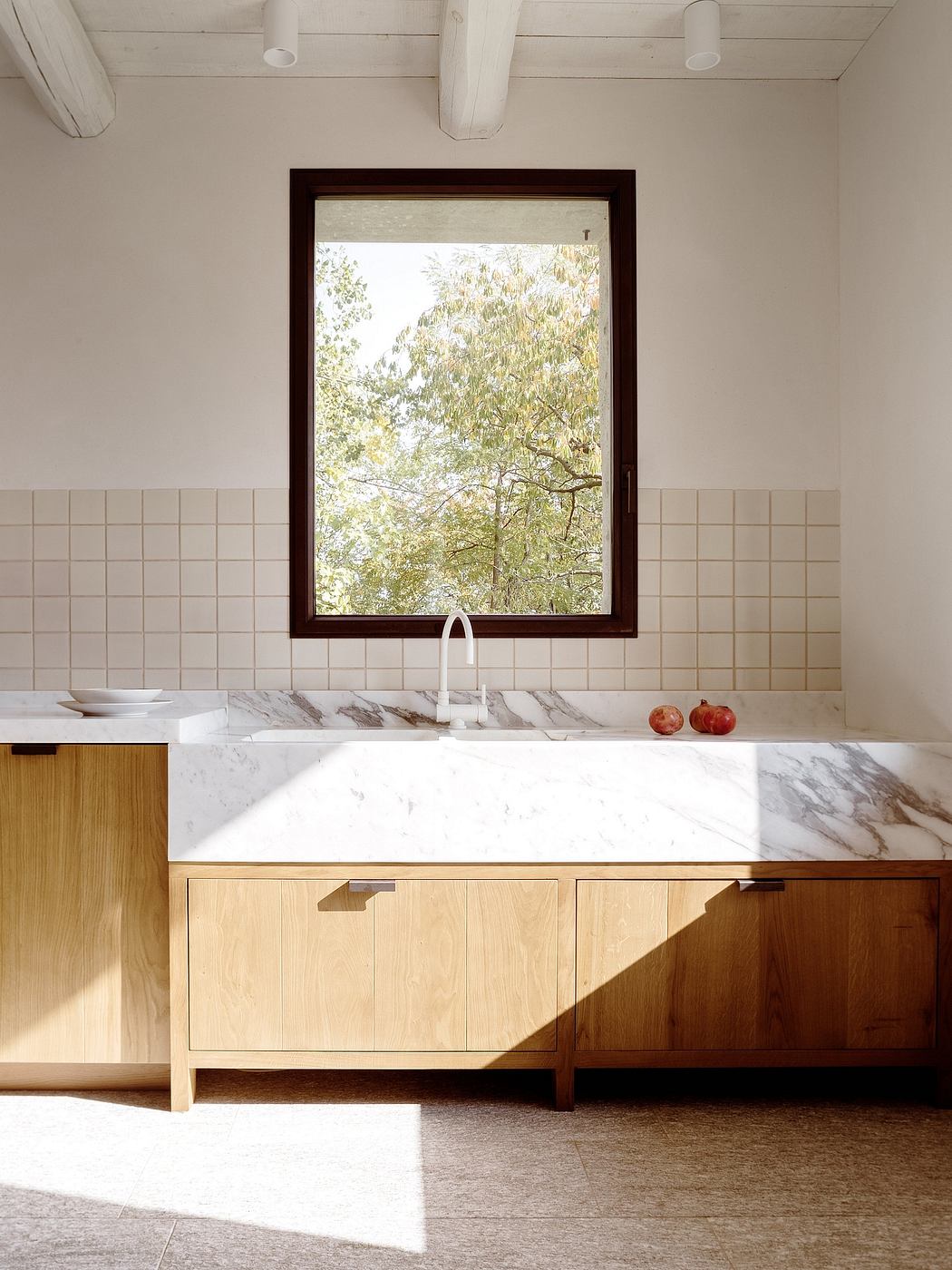Bright kitchen with wooden cabinets, marble countertop, and large window overlooking nature.