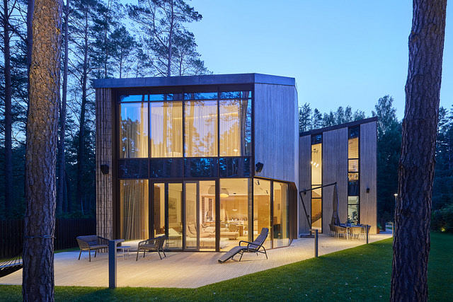 Modern glass and wood structure with open outdoor seating area in wooded setting.