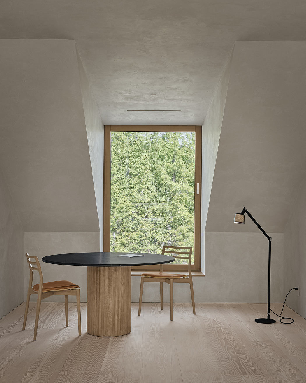 Minimalist dining nook with wooden table, chairs, and large window overlooking lush greenery.