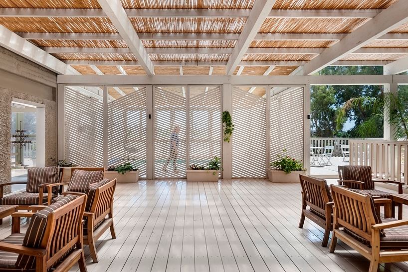 An airy, covered patio with slatted wood ceiling and plush seating, overlooking a lush outdoor area.