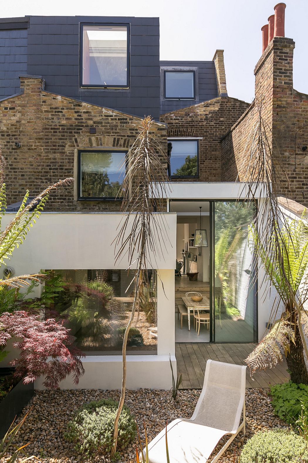 Striking modern extension blending old brick and glass, with lush landscaped garden.