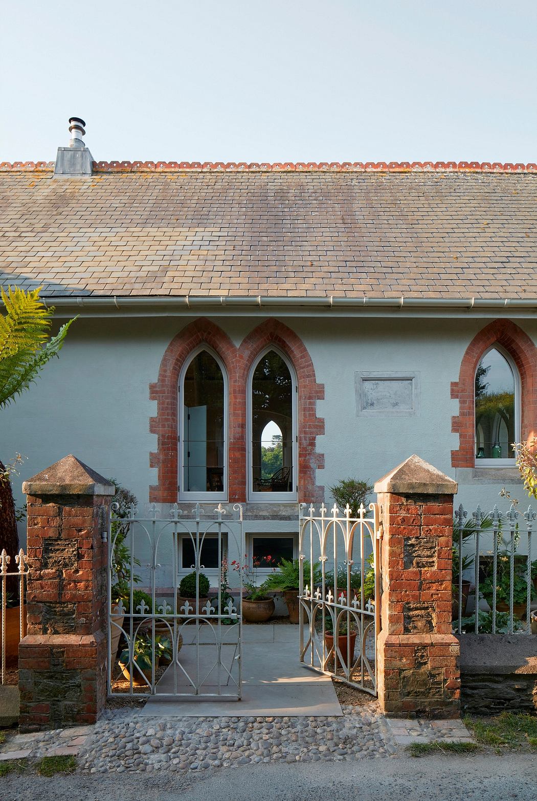 A quaint brick building with ornate arched windows and a tile roof, surrounded by lush greenery.