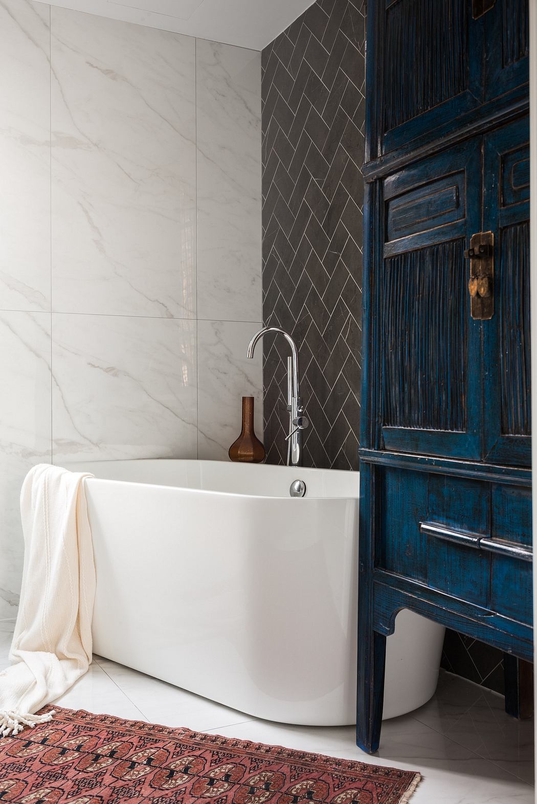Contemporary bathroom with white freestanding tub, patterned tile, and antique wood cabinet.
